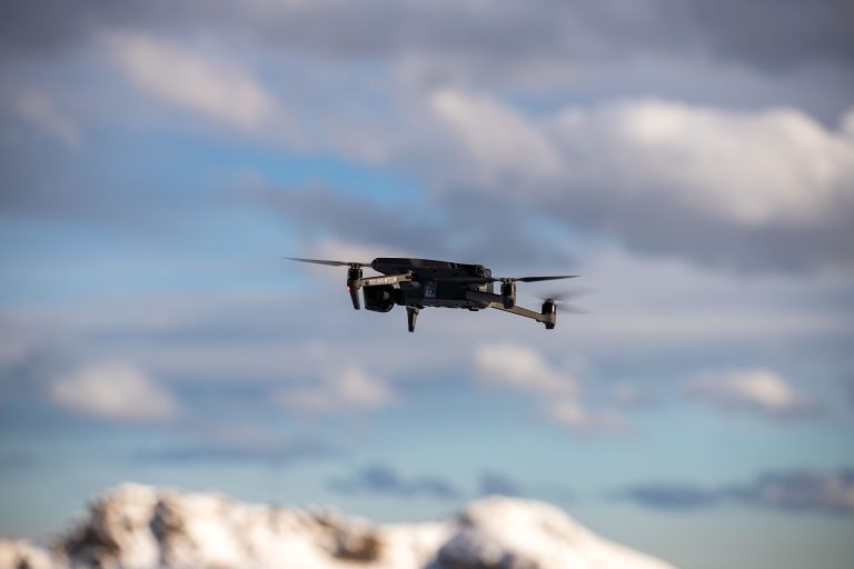 Aerial view of a drone flying over snow-covered mountains with dramatic clouds