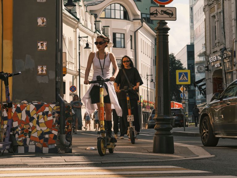 Two women riding electric scooters on a city street, showcasing urban commute