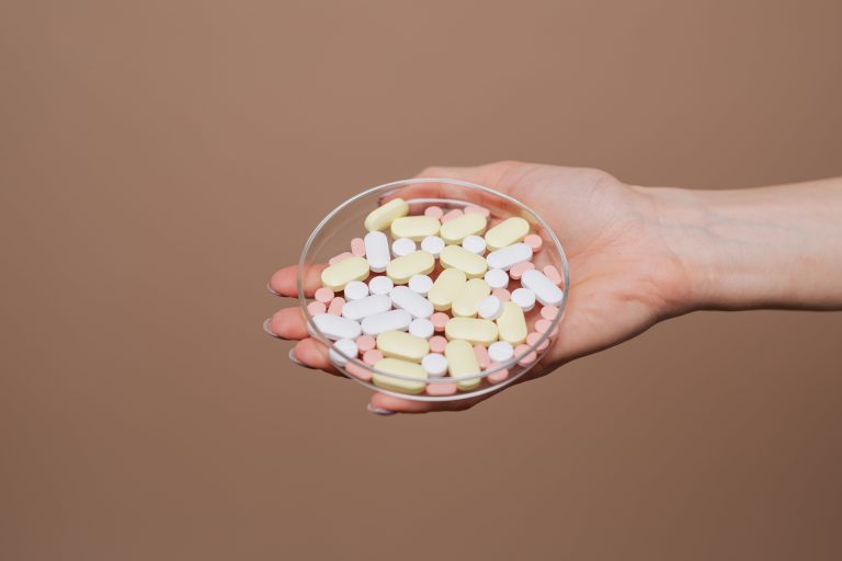 A hand holding a petri dish of tablets