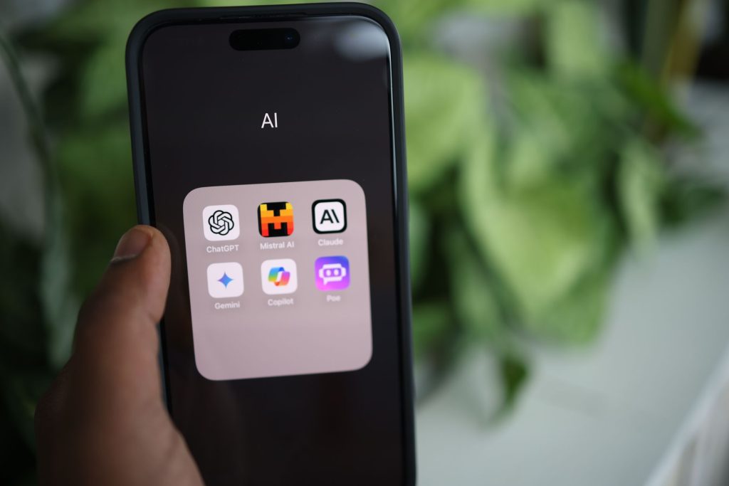 A hand holding a smartphone with a folder of AI apps on screen