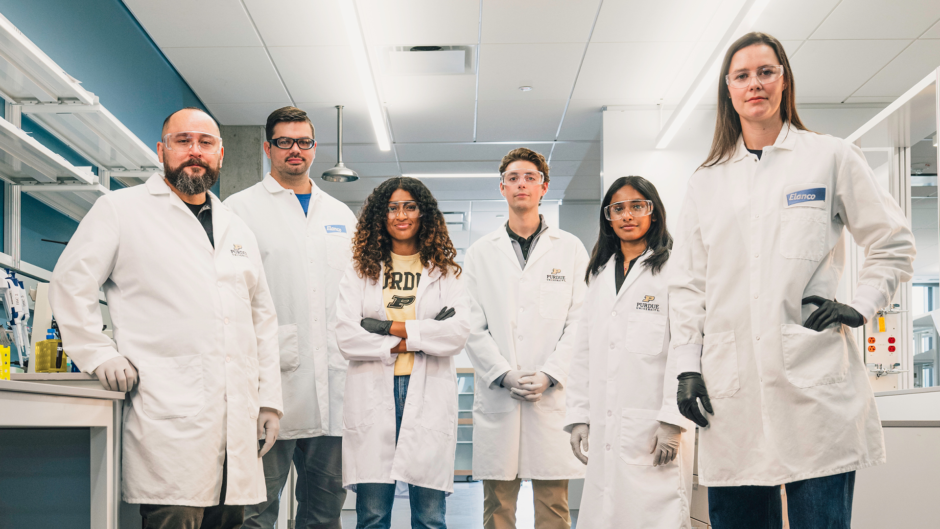 Researchers in lab coats and protective eyewear stand together in a laboratory