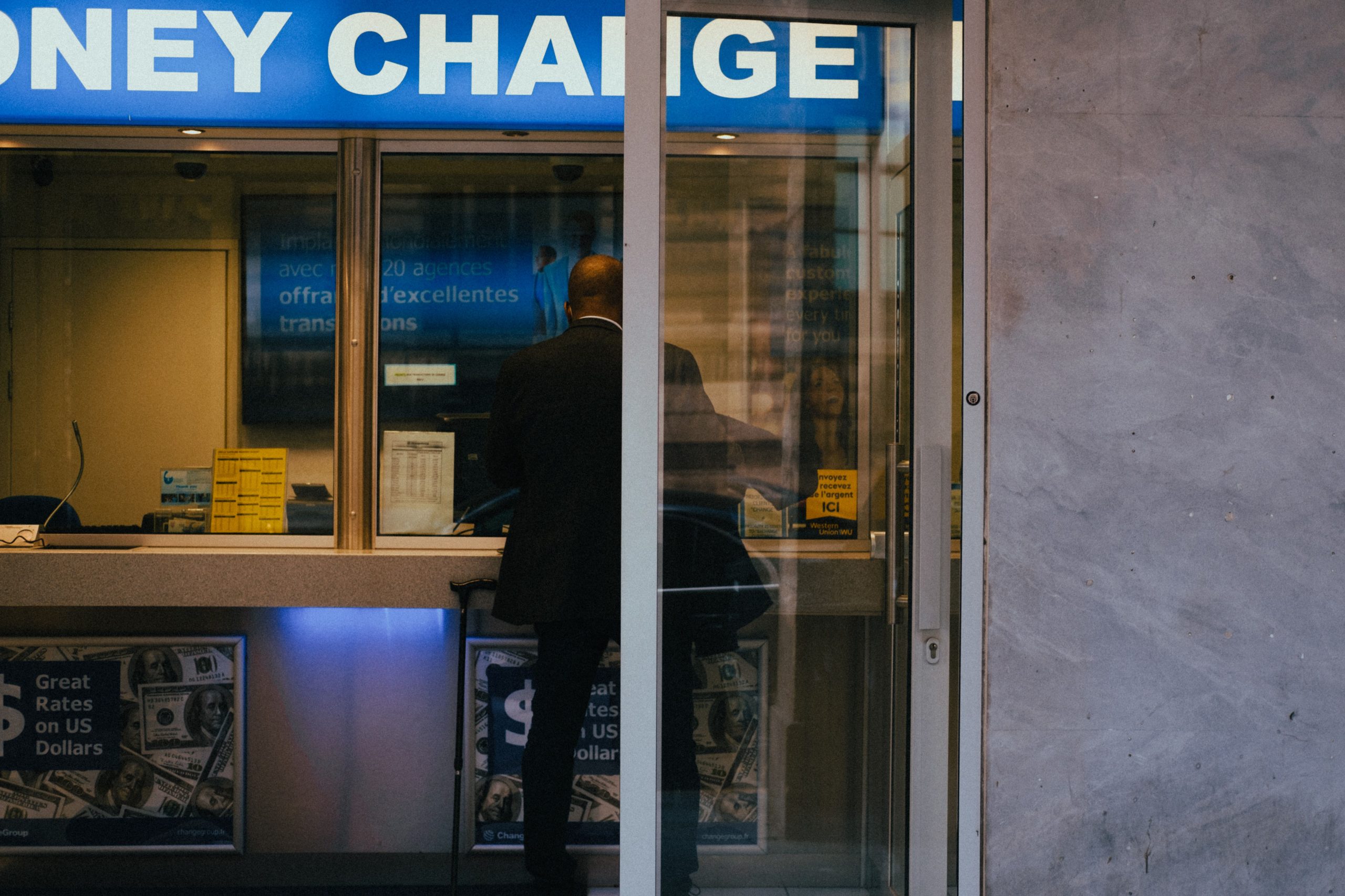 Man at a currency exchange office window, showing currency rates inside a bustling city