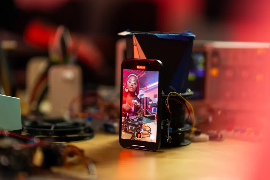 Black woman live streaming tech video on smartphone in an electronics workshop