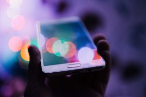 A hand holds a smartphone against colorful blurred lights